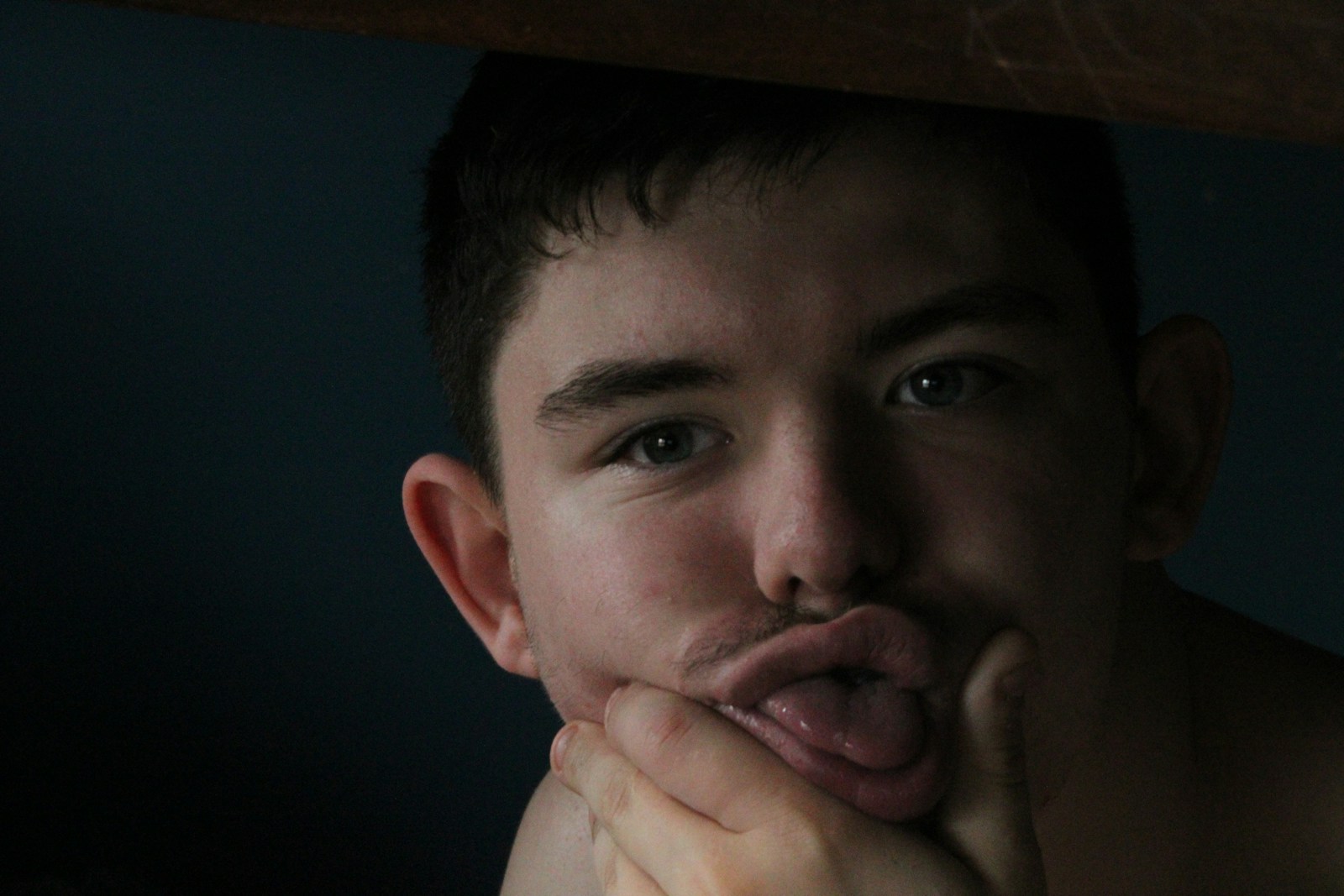 An adult resting their chin on a hand in soft dark light.