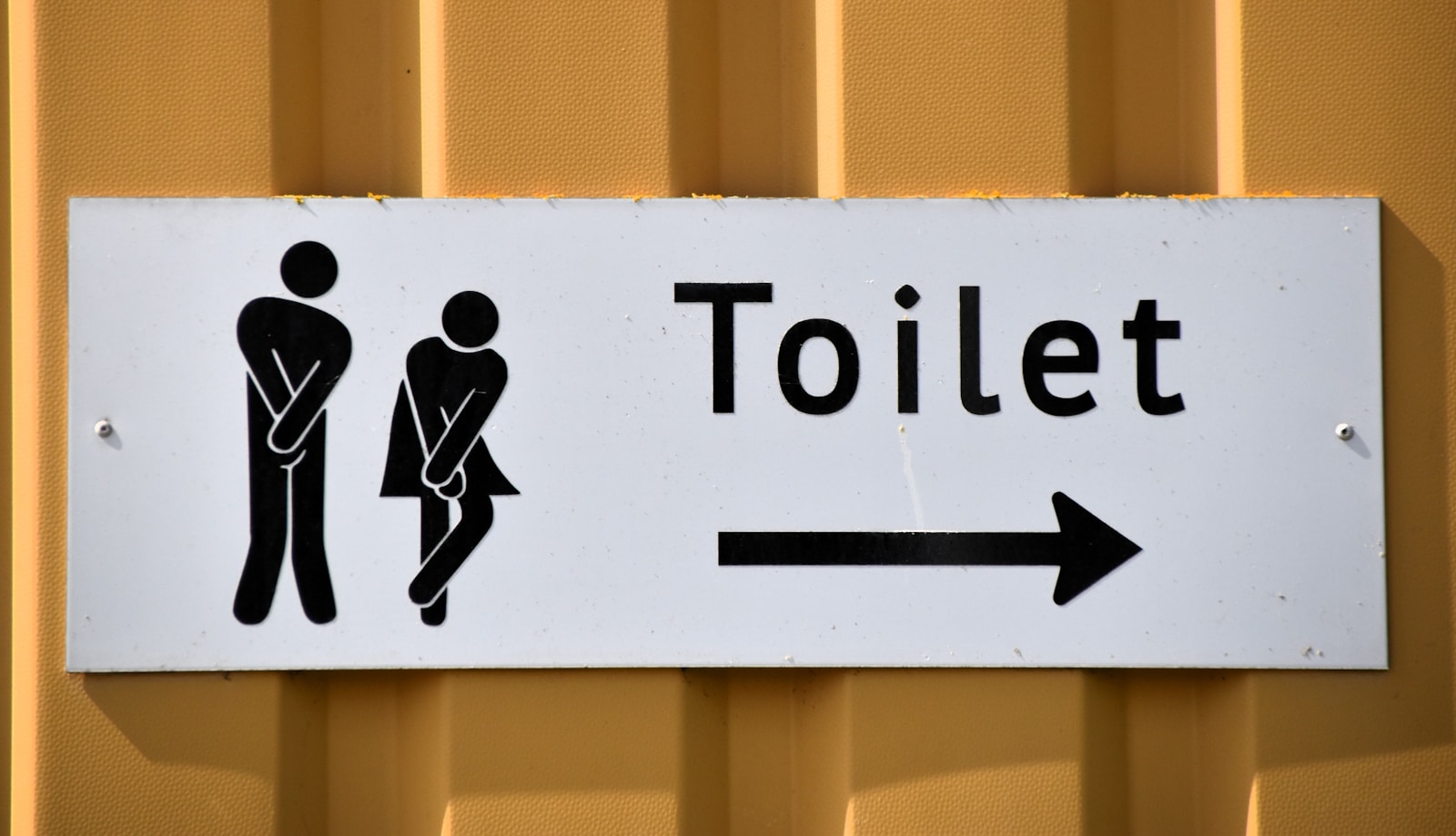 A yellow-backed toilet sign with figures and an arrow.