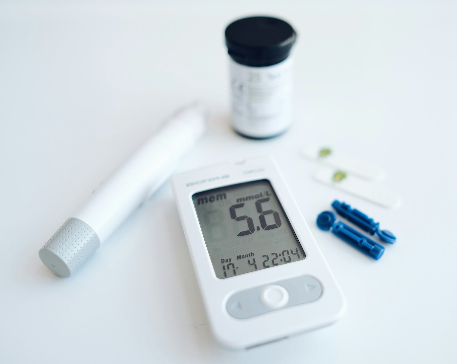 A glucose meter, a lancing device and small medical supplies on a table.