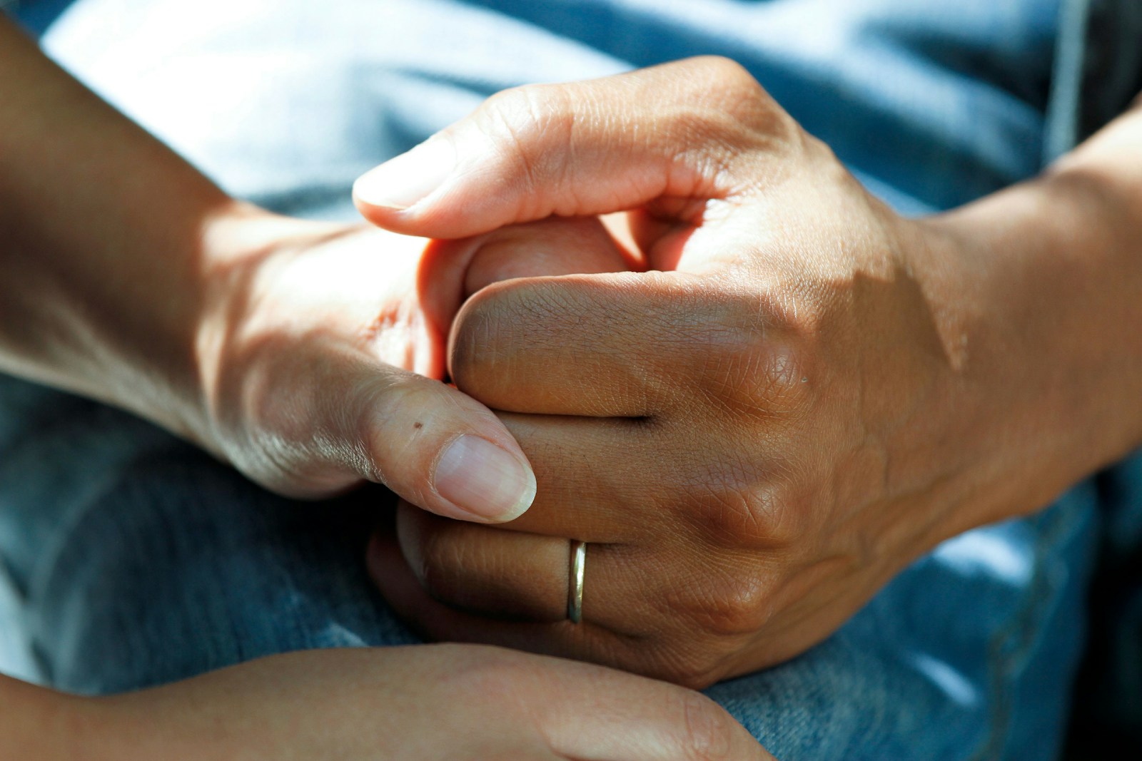 Close view of clasped hands resting on a lap covered in blue fabric.