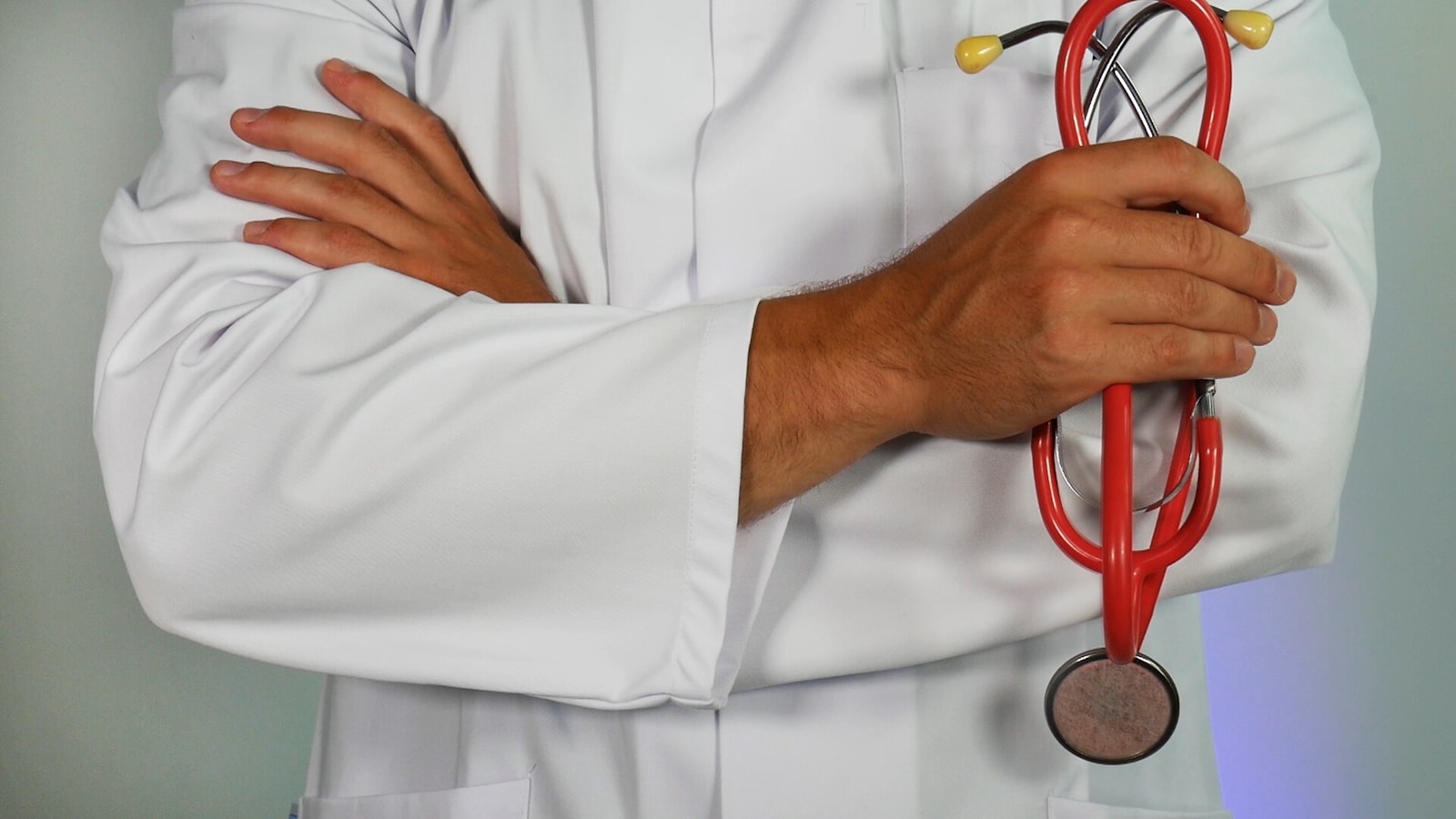 Cropped torso of a person in a white medical coat holding a red stethoscope.