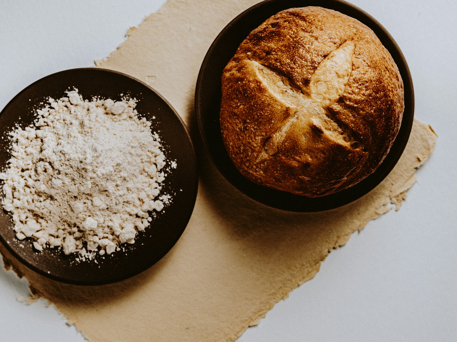Overhead view of flour in one bowl and a round rustic loaf in another.