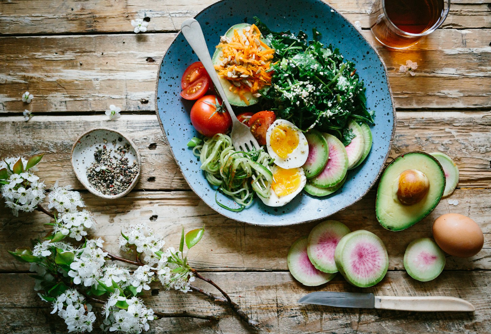 Overhead plate with leafy greens, egg, avocado and other foods on a wooden table.