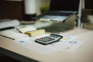 Calculator on paperwork beside a notebook and laptop