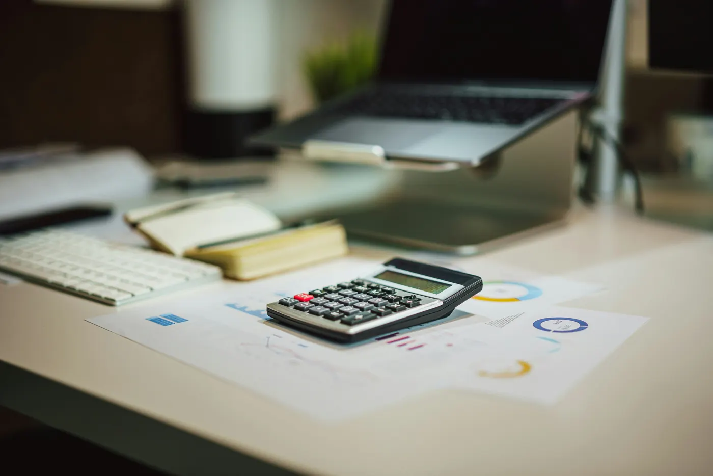 Calculator, paperwork, notebook and laptop on a desk.