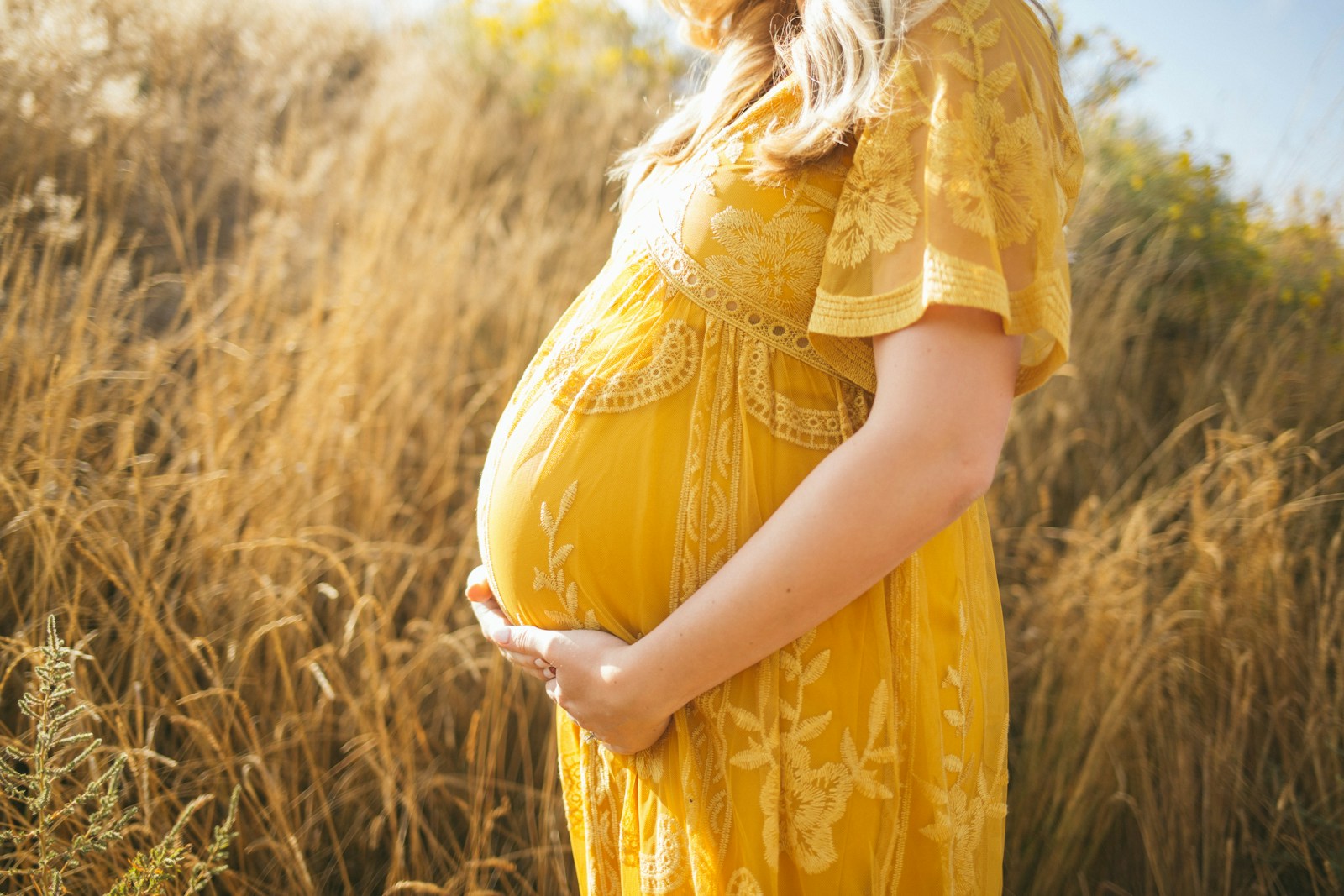 Adult with a visible pregnant abdomen outdoors in a yellow dress