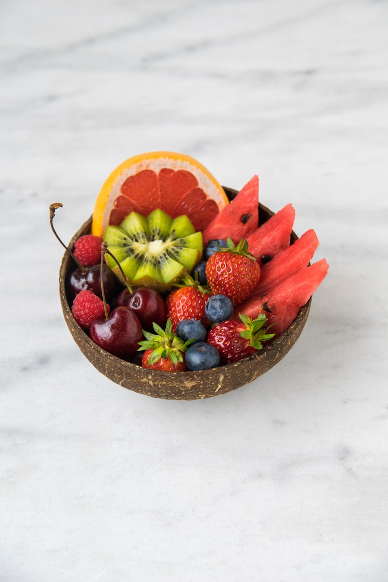 A bowl of assorted cut fruit and berries on a light surface.