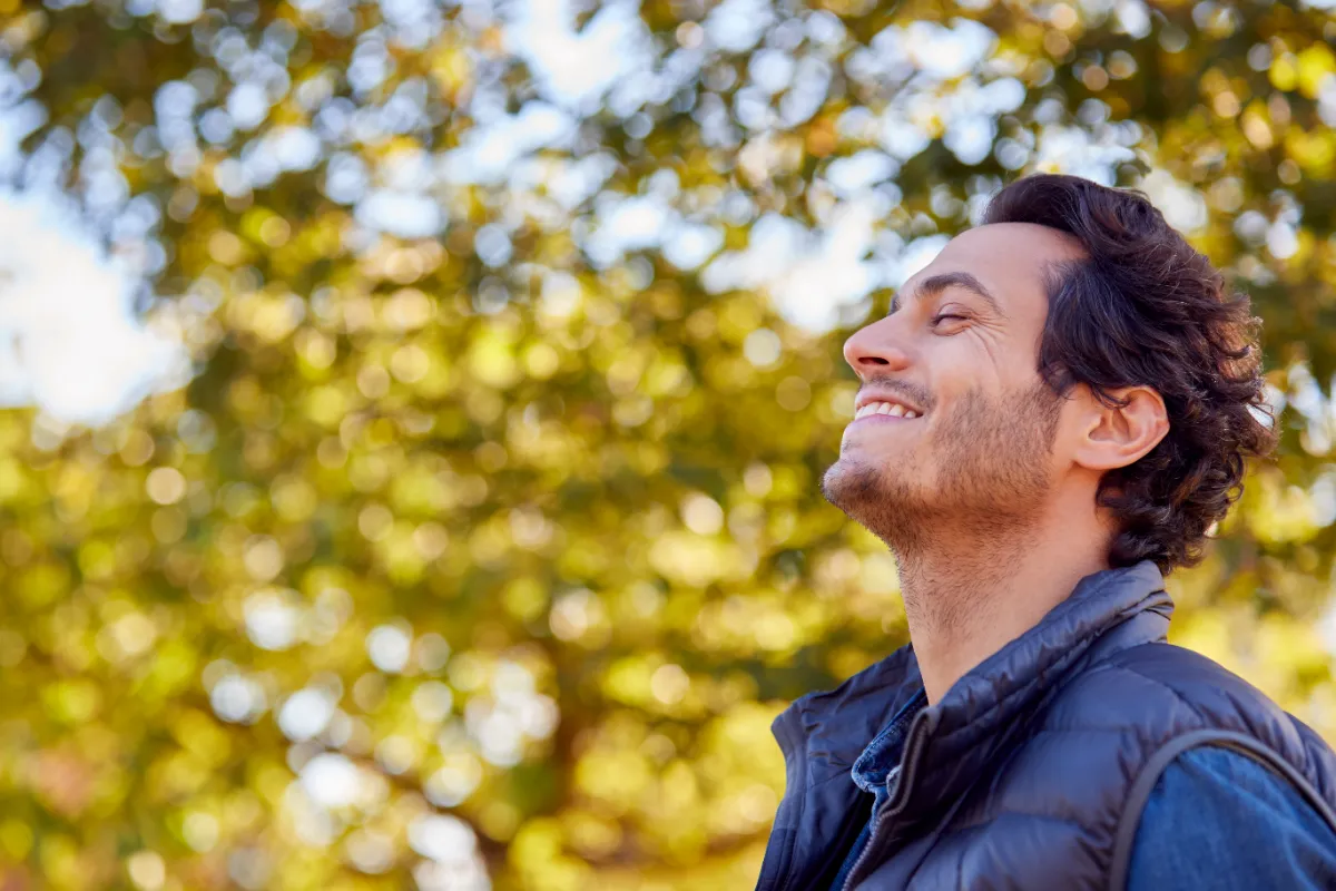 An adult outdoors with eyes closed and face toward the light