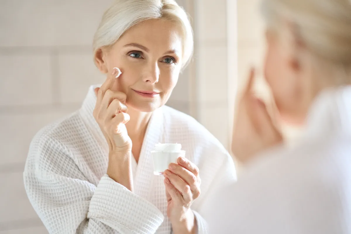 Mature woman applying cream while looking in a mirror