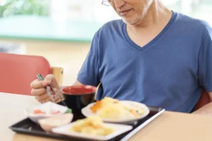 older man eating lunch with chopsticks indoors utc