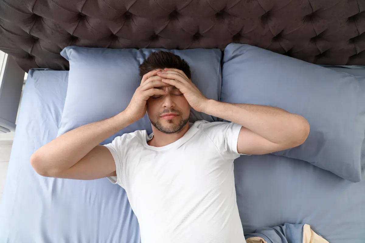 Man lying in bed with his hands over his face