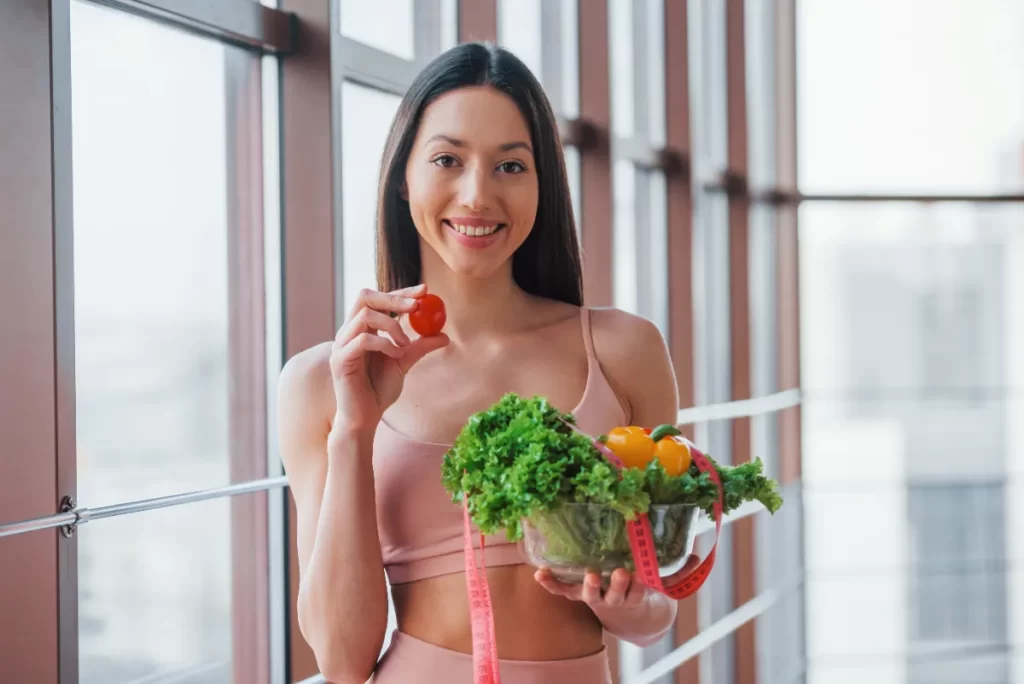 woman holding vegetables and a tomato indoors utc