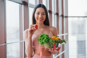 woman holding vegetables and a tomato indoors utc