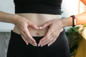 woman making heart shape over stomach indoors utc