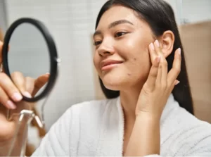 young woman examining her skin in mirror utc