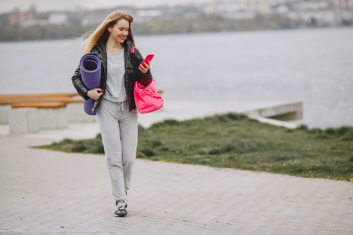 active woman walking with yoga mat and phone utc