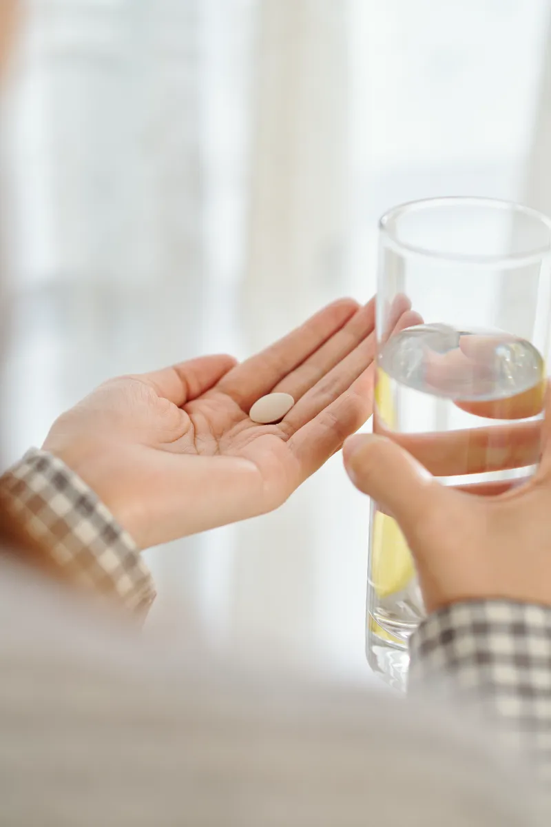 An adult holding a small tablet beside a glass of water.