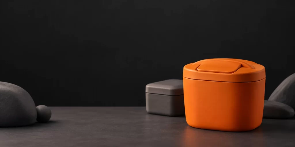 Original AI-generated editorial image: Conceptual tangerine clay sharps container with a closed lid against charcoal.