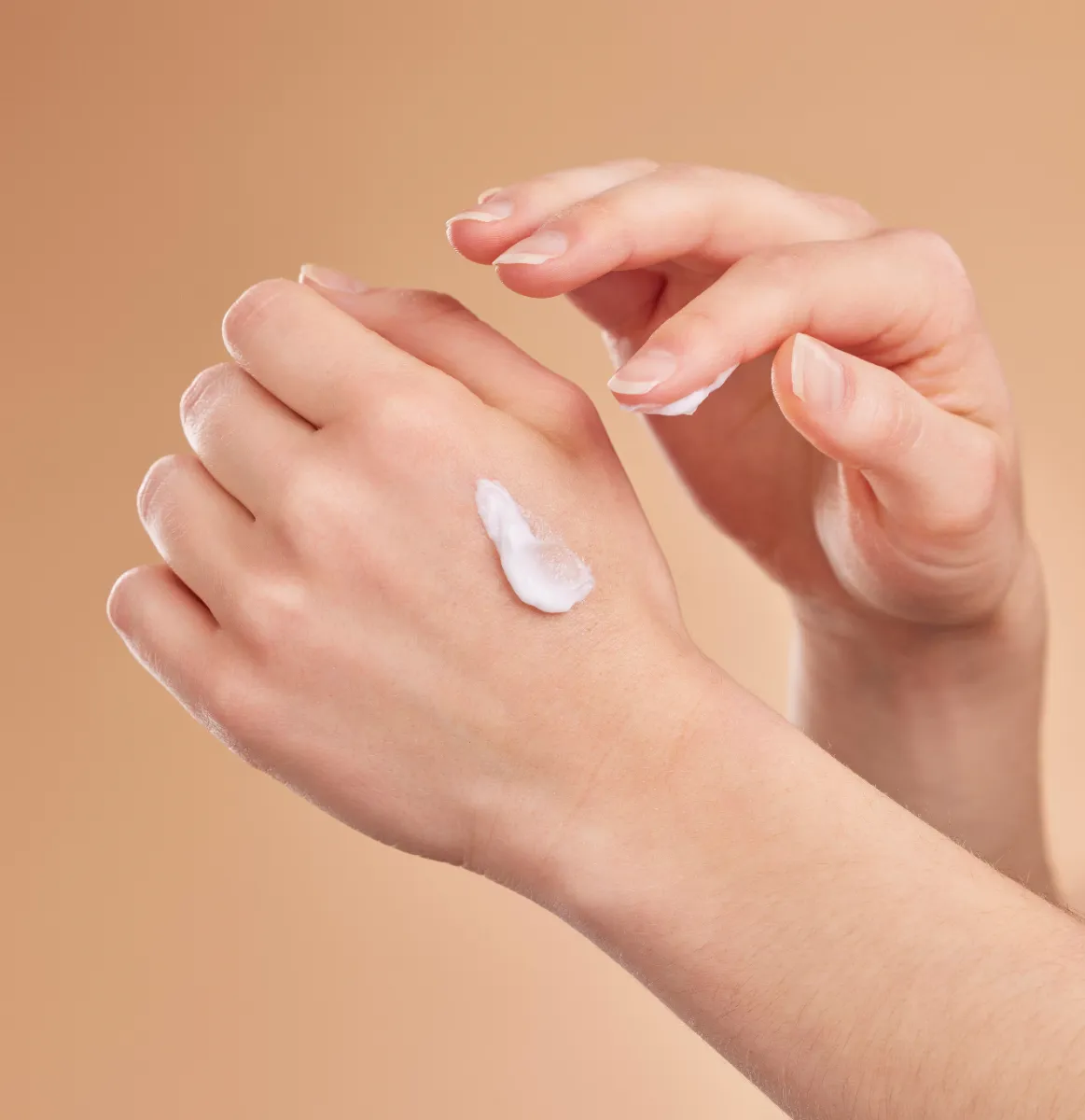 Hands applying cream to the back of a hand.