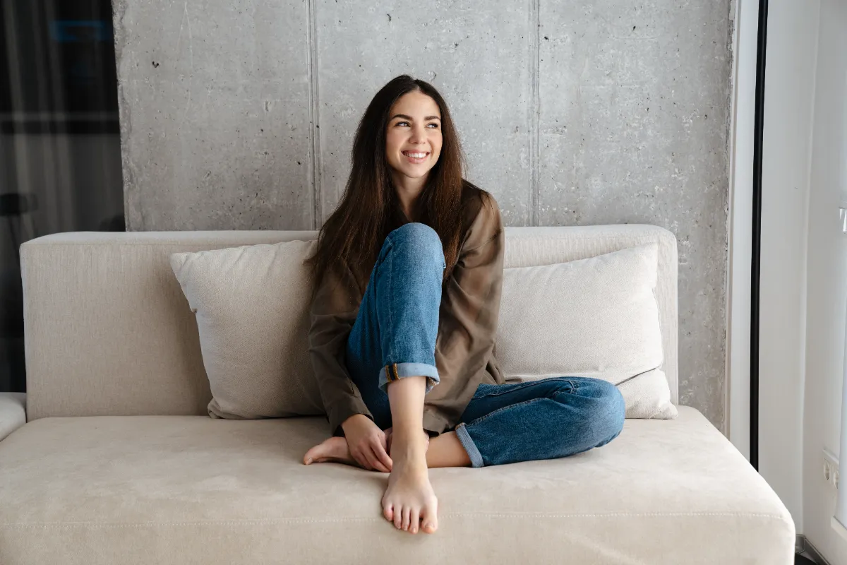 An adult seated on a beige sofa with legs folded.