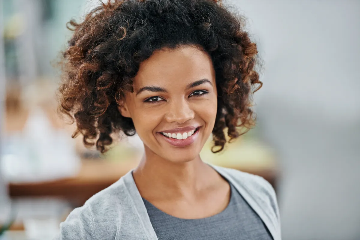 An adult with curly hair wearing a gray cardigan indoors.