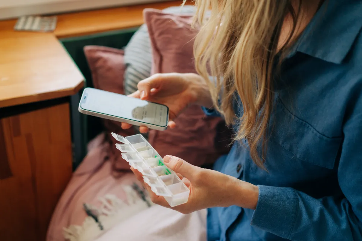 An adult checking a phone while holding a weekly pill organizer.