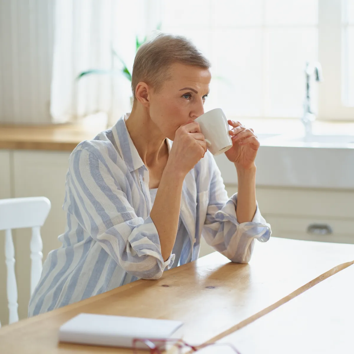 An adult man in striped sleepwear holds a mug beside a kitchen counter.
