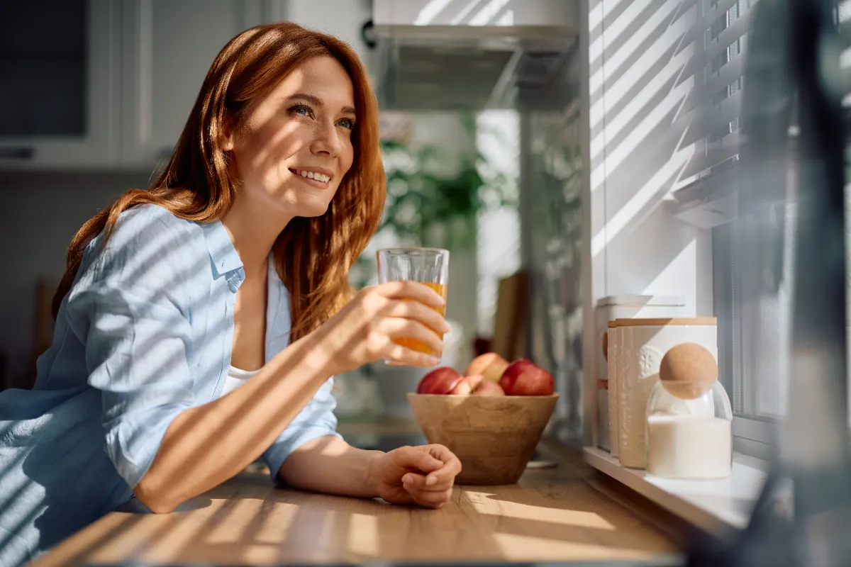An adult at a kitchen table with a glass of orange juice and a fruit bowl.