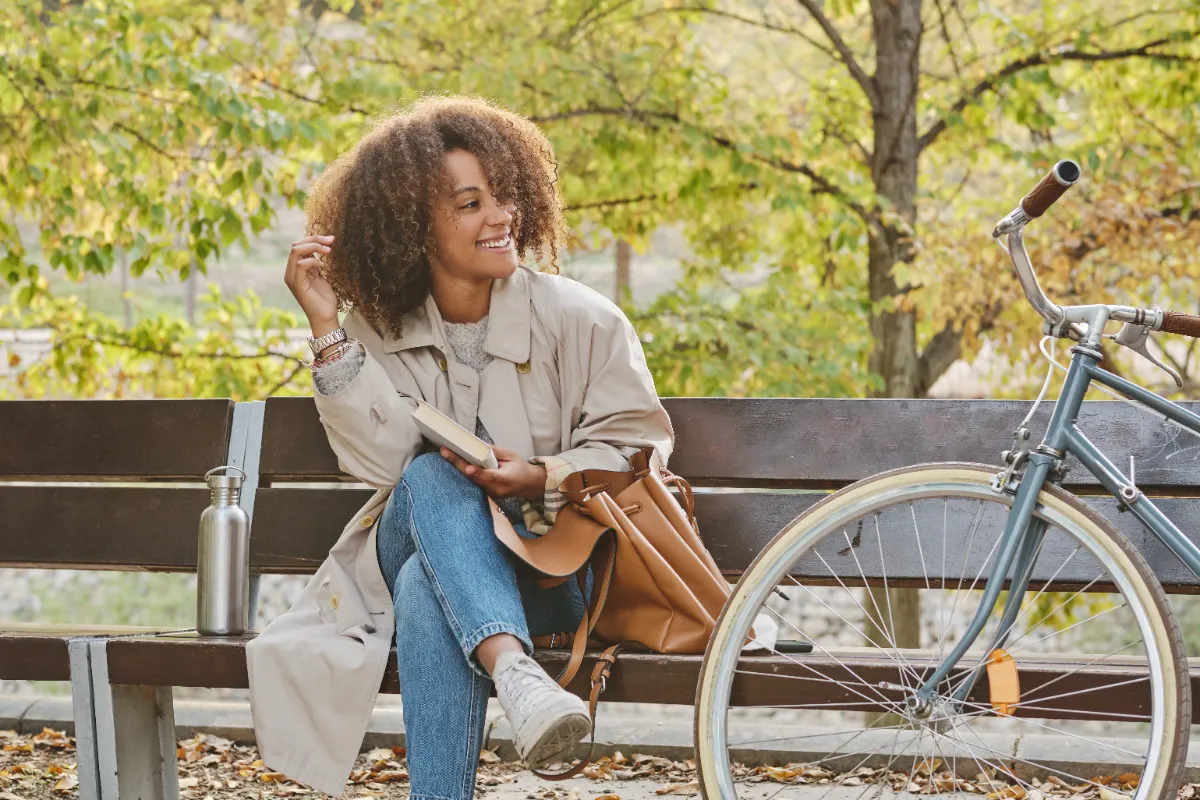 An adult seated on an outdoor bench beside a bicycle.