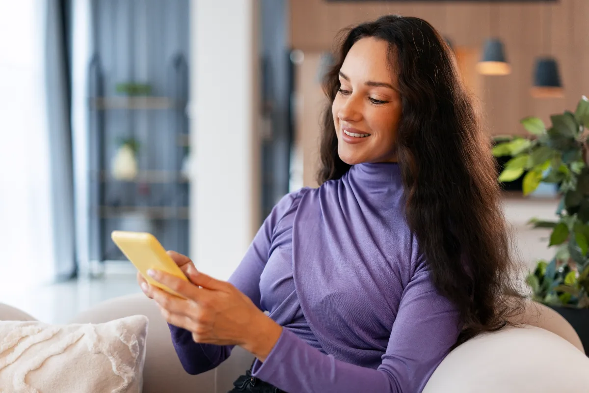 An adult reading a smartphone while seated on a sofa.