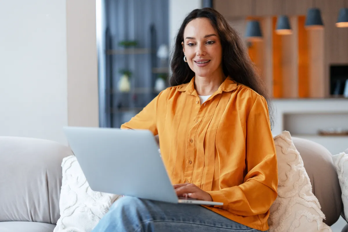 A woman works on a laptop from a sofa.