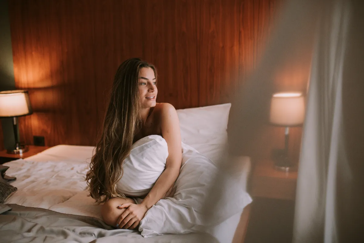 woman wrapped in sheets sitting on bed utc