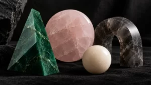 Jade stone prism, pale-rose disk, smoky-gray arch and cream sphere arranged on black felt in a conceptual sculpture photograph.