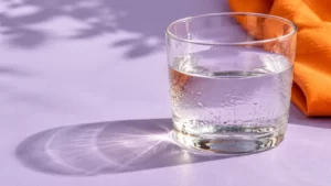 A clear water glass with condensation against lilac and orange.