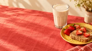 A protein drink beside toast and strawberries on a coral-red table.