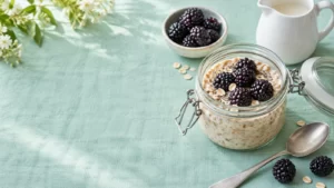 A jar of soaked oats and blackberries beside a white pitcher on mint linen.