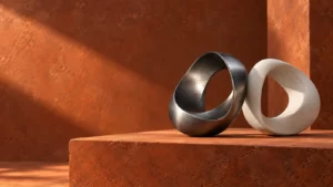 Gunmetal and pale-stone sculptural loops resting on a rust-colored clay plinth.