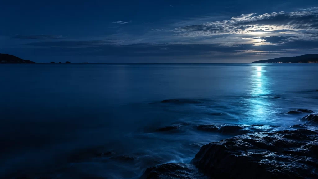 Midnight-blue coastal horizon with cyan reflected light at dusk.