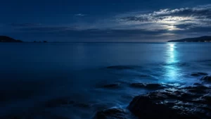 Midnight-blue coastal horizon with cyan reflected light at dusk.