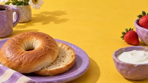 A bagel, yogurt and strawberries on yellow and lilac ceramics.