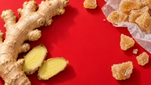 Ginger root and unbranded ginger sweets arranged on a cherry-red surface.