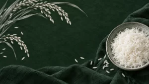 A bowl of white rice beside silver botanical drawings on forest-green fabric.