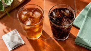 Two glasses containing amber and dark drinks on orange tile beside a mint-colored napkin.