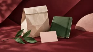 Forest-green notebook, folded ivory bag and blush card against burgundy paper.